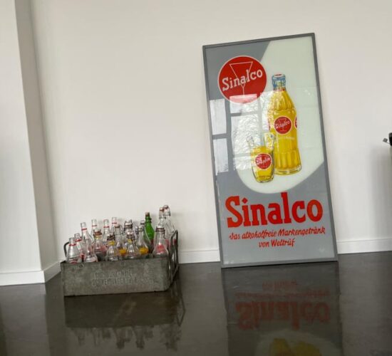 Foto von leeren Pfandflaschen und ein eingerahmtes Bild mit einem Werbeslogan von Sinalco